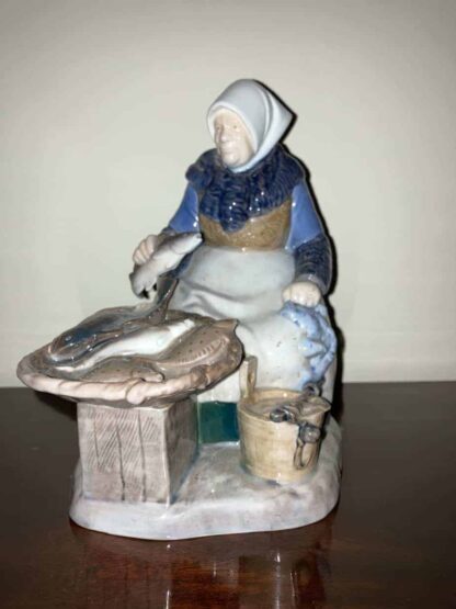 Elderly woman, wearing a headscarf, siting behind a small table and bucket both of which contain fish