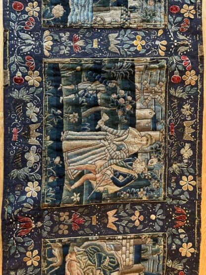 Second panel of needlework showing a couple walking together in a garden